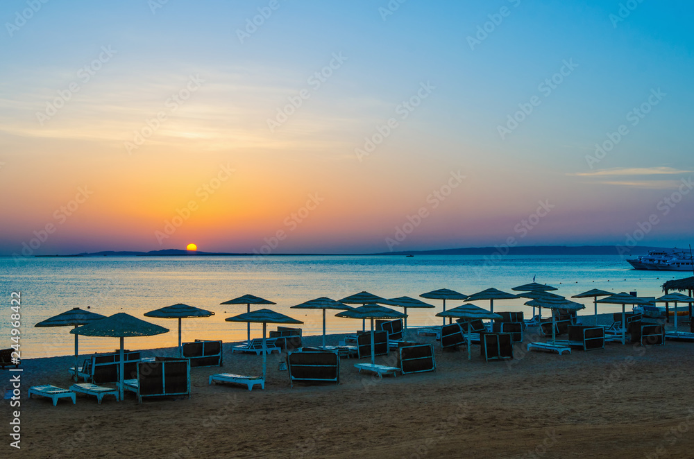 Sunrise, sunset on the beach with umbrellas orange and blue color at dusk.