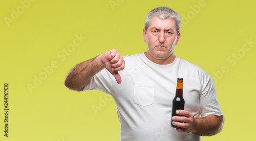 Handsome senior man drinking beer bottle over isolated background with angry face, negative sign showing dislike with thumbs down, rejection concept