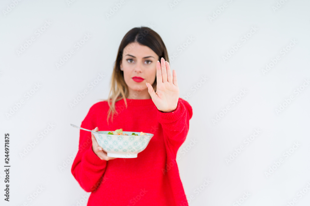 Young woman eating fresh healthy salad over isolated background with open hand doing stop sign with serious and confident expression, defense gesture Young woman eating fresh healthy salad over isolated background with open hand doing stop sign with serious and confident expression, defense gesture