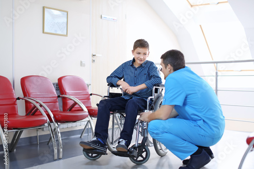 Male doctor taking care of little boy in wheelchair indoors