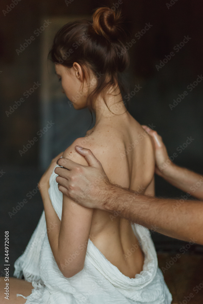 Naklejka premium Professional male masseur doing massage for woman client at spa salon, studio. Warm romantic illumination, low key. Wellness, relaxation and healthcare concept