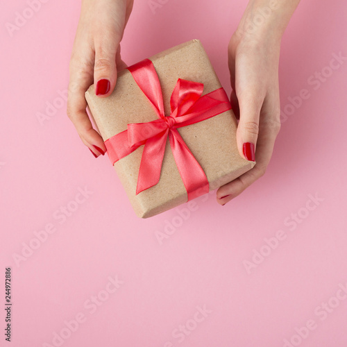 girl holding a present in hands, women with gift box in hands wrapped in decorative paper on pink background, top view, concept holiday and gifts