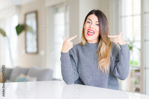 Young beautiful woman wearing winter sweater at home smiling confident showing and pointing with fingers teeth and mouth. Health concept.