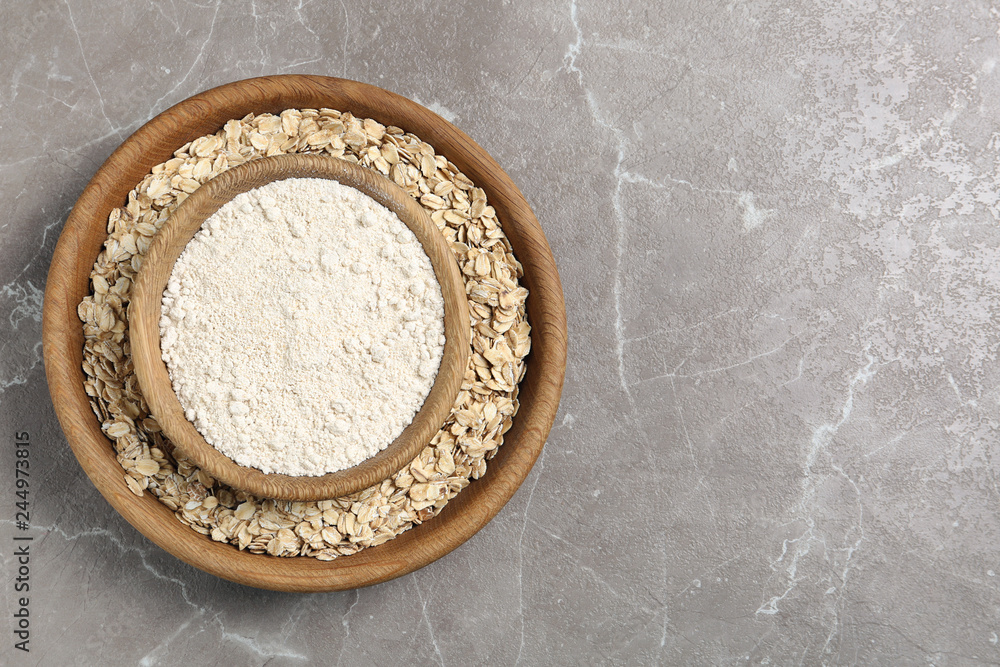 Bowls with oat flour and flakes on grey background, top view. Space for text Bowls with oat flour and flakes on grey background, top view. Space for text