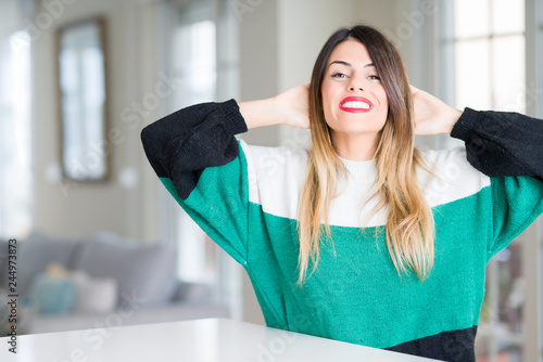 Young beautiful woman wearing winter sweater at home Relaxing and stretching with arms and hands behind head and neck, smiling happy