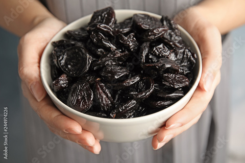 Woman holding bowl of dried plums, closeup. Healthy fruit