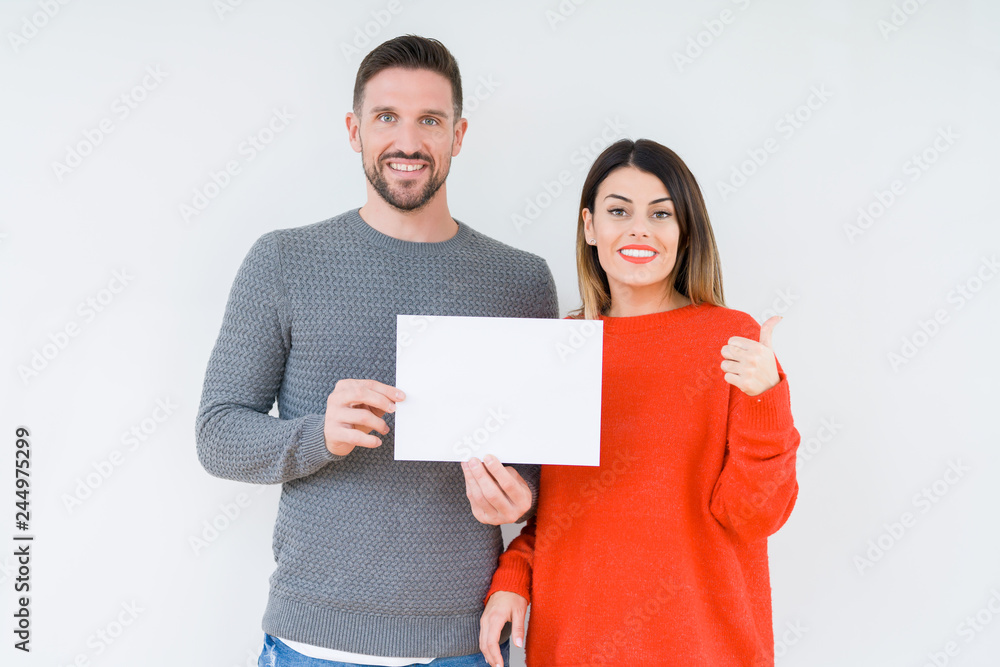 Young couple holding blank sheet paper over isolated background pointing and showing with thumb up to the side with happy face smiling Young couple holding blank sheet paper over isolated background pointing and showing with thumb up to the side with happy face smiling