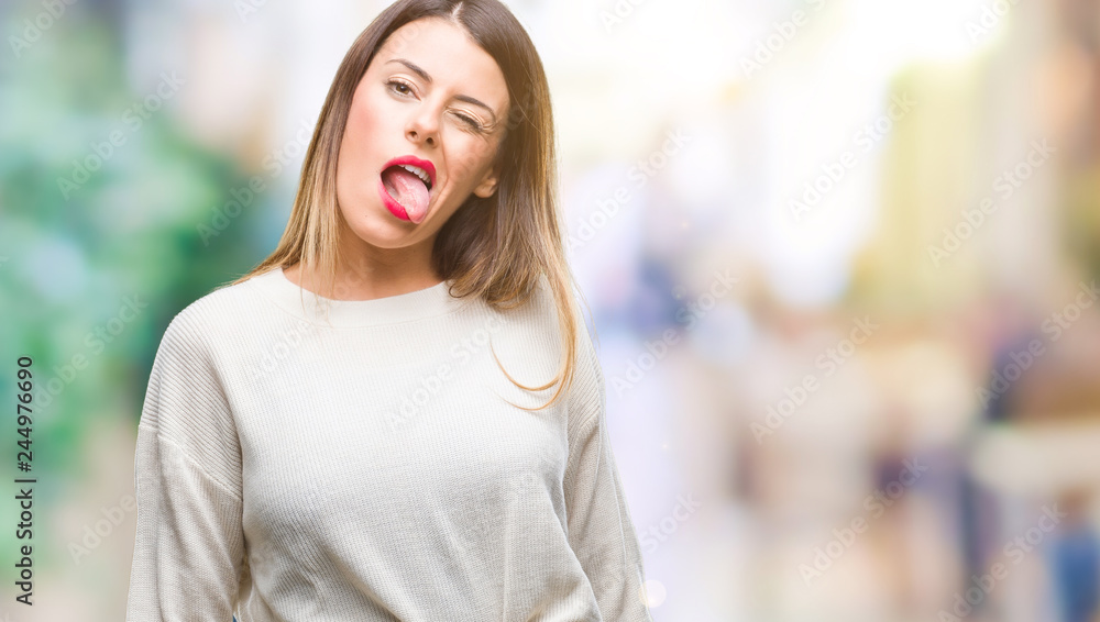 Young beautiful woman casual white sweater over isolated background sticking tongue out happy with funny expression. Emotion concept.
