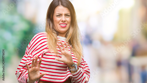 Young beautiful woman casual stripes winter sweater over isolated background disgusted expression, displeased and fearful doing disgust face because aversion reaction. With hands raised
