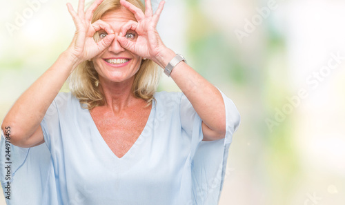 Middle age blonde business woman over isolated background doing ok gesture like binoculars sticking tongue out, eyes looking through fingers. Crazy expression.