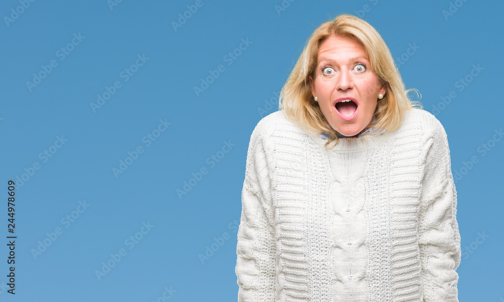 Middle age blonde woman wearing winter sweater over isolated background afraid and shocked with surprise expression, fear and excited face. Middle age blonde woman wearing winter sweater over isolated background afraid and shocked with surprise expression, fear and excited face.