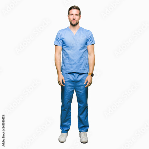 Handsome doctor man wearing medical uniform over isolated background with serious expression on face. Simple and natural looking at the camera.