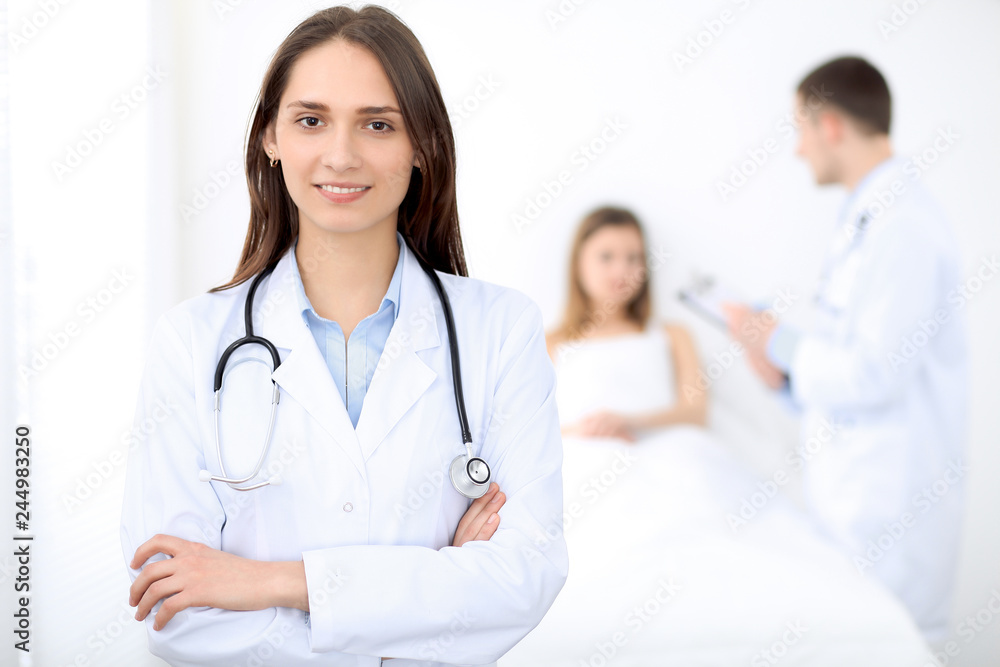 Medicine doctor standing and smiling on the background with patient in the bed Medicine doctor standing and smiling on the background with patient in the bed
