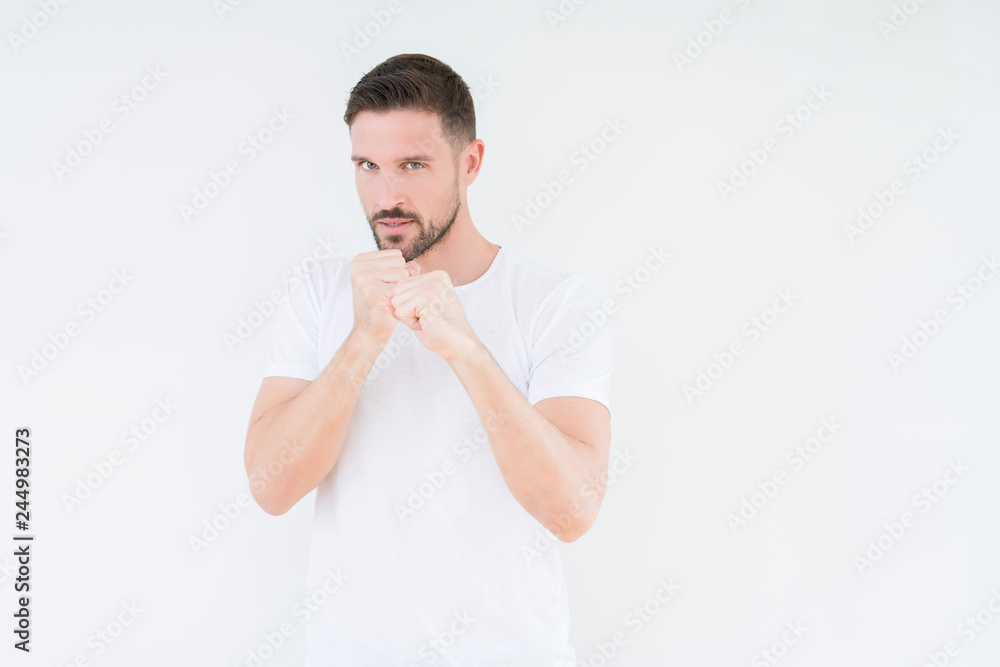 Young handsome man wearing casual white t-shirt over isolated background Ready to fight with fist defense gesture, angry and upset face, afraid of problem Young handsome man wearing casual white t-shirt over isolated background Ready to fight with fist defense gesture, angry and upset face, afraid of problem