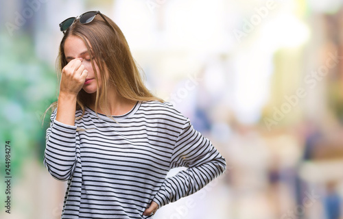 Young beautiful blonde woman wearing sunglasses over isolated background tired rubbing nose and eyes feeling fatigue and headache. Stress and frustration concept.