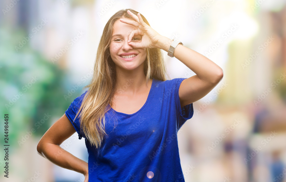 Young beautiful blonde woman over isolated background doing ok gesture with hand smiling, eye looking through fingers with happy face.