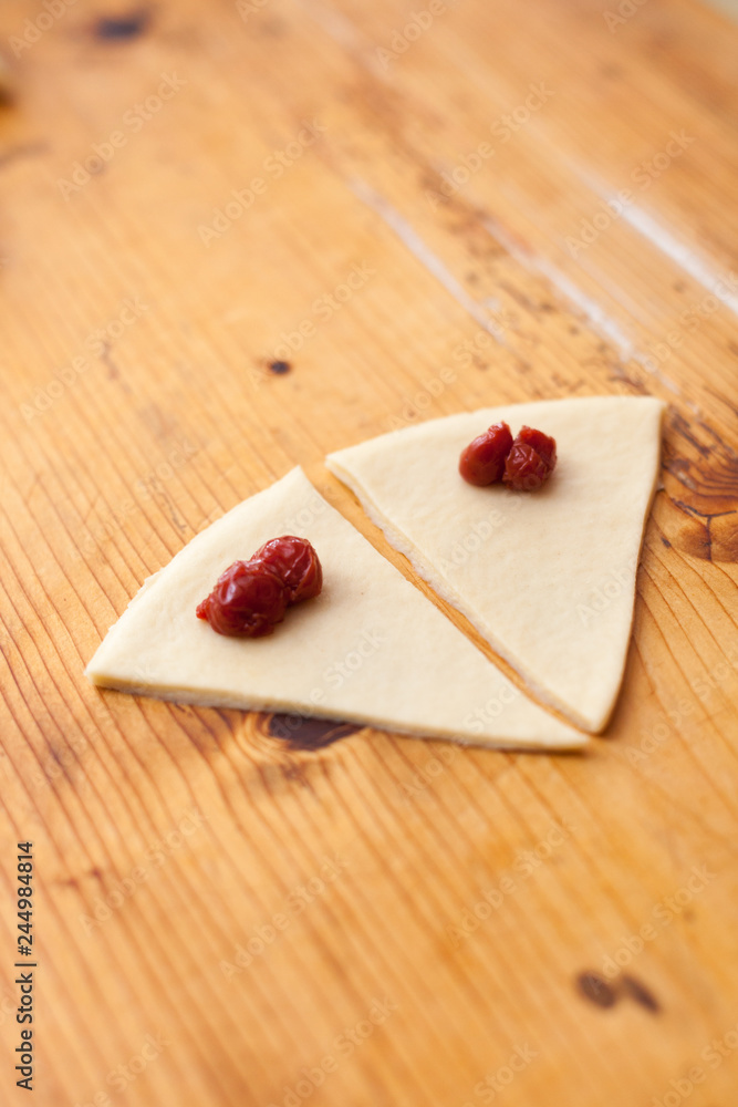 Process of cooking small croissants with cherry for breakfast. Pieces of dough with cherry filling. Preparation of baking on a rustic wooden background Process of cooking small croissants with cherry for breakfast. Pieces of dough with cherry filling. Preparation of baking on a rustic wooden background