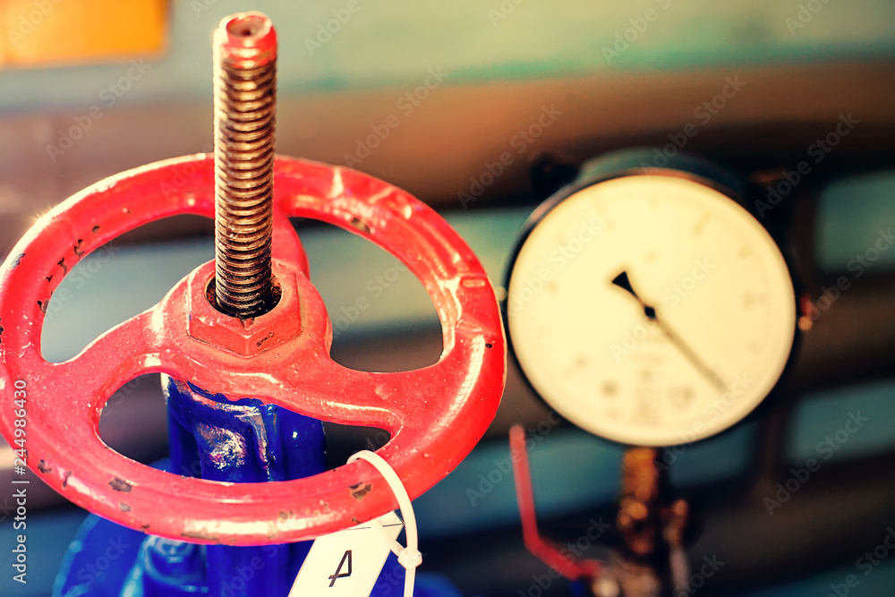 Red gas valve and pressure gauge with an arrow on the limit. Background for gasification. Close up.