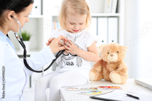 Doctor and patient baby in hospital. Little girl is being examined by pediatrician with stethoscope. Health care, insurance and help concept photo