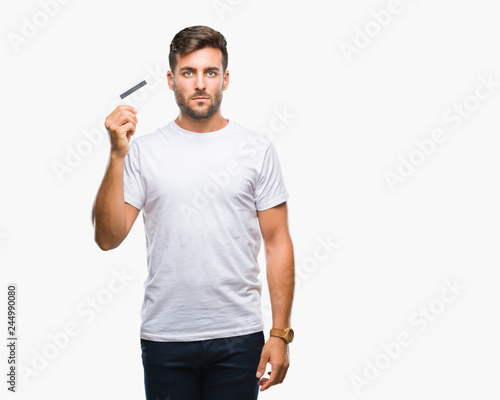 Young handsome man holding credit card over isolated background with a confident expression on smart face thinking serious