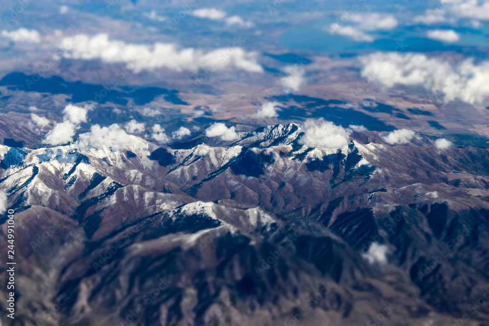 Aerial view of large snow capped mountains surrounded by dry desert Aerial view of large snow capped mountains surrounded by dry desert