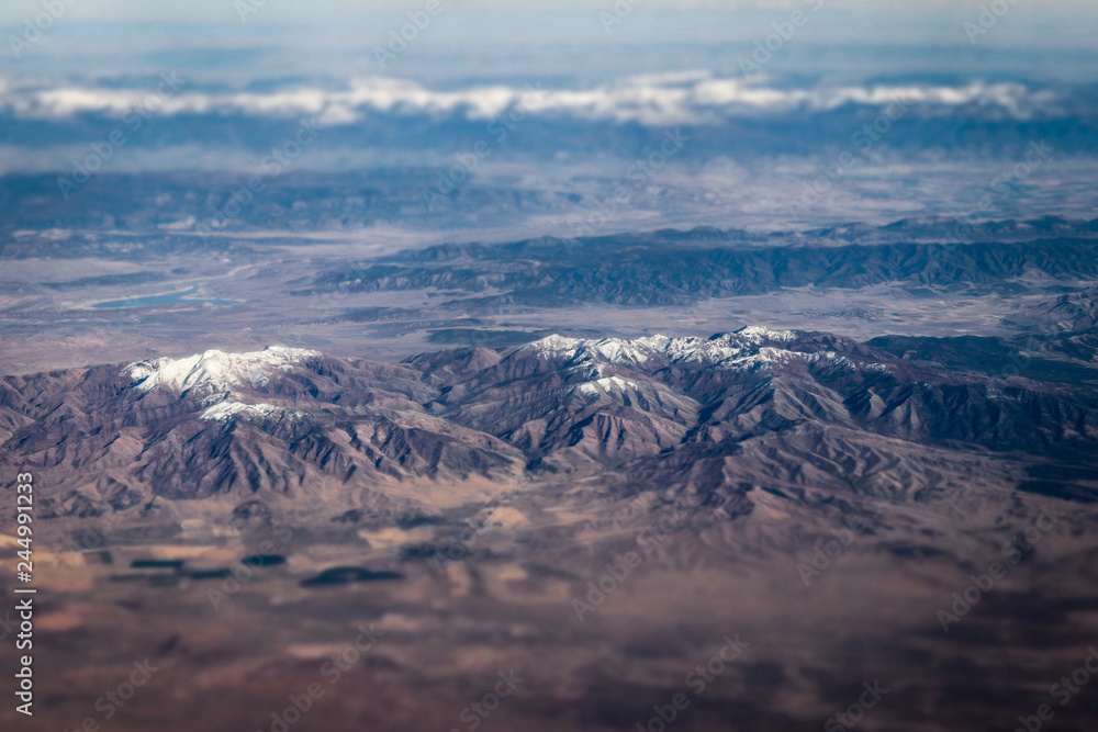 Aerial view of large snow capped mountains surrounded by dry desert