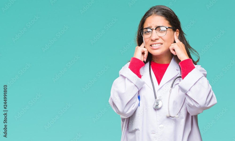 Young arab doctor woman over isolated background covering ears with fingers with annoyed expression for the noise of loud music. Deaf concept. Young arab doctor woman over isolated background covering ears with fingers with annoyed expression for the noise of loud music. Deaf concept.