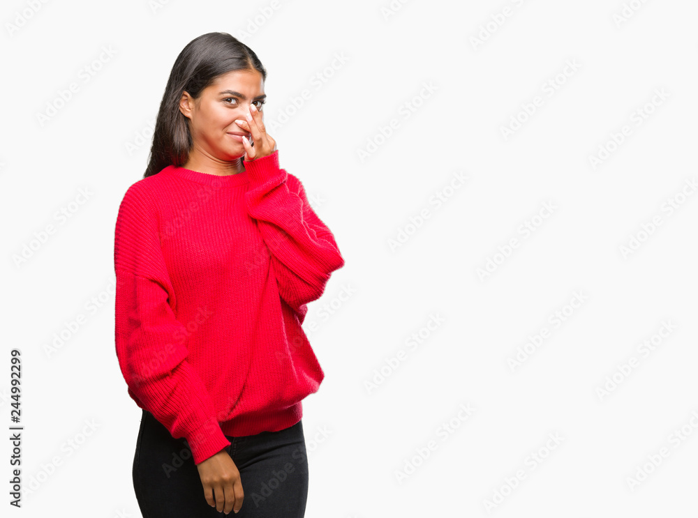 Young beautiful arab woman wearing winter sweater over isolated background smelling something stinky and disgusting, intolerable smell, holding breath with fingers on nose. Bad smells concept.
