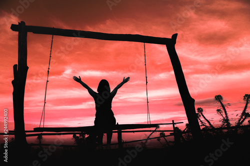 Silhouette of a woman having fun sitting on swing at sundown with beautiful clouds in background,Freedom and happiness for travel concept