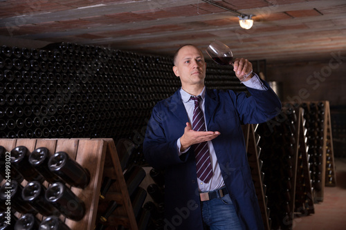 Wine producer inspecting quality of red wine in winery vault photo