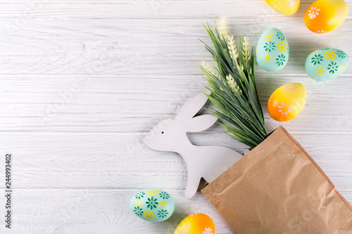 Photography Easter composition with craft paper package, colorful easter eggs, decorative wooden bunny and flowers