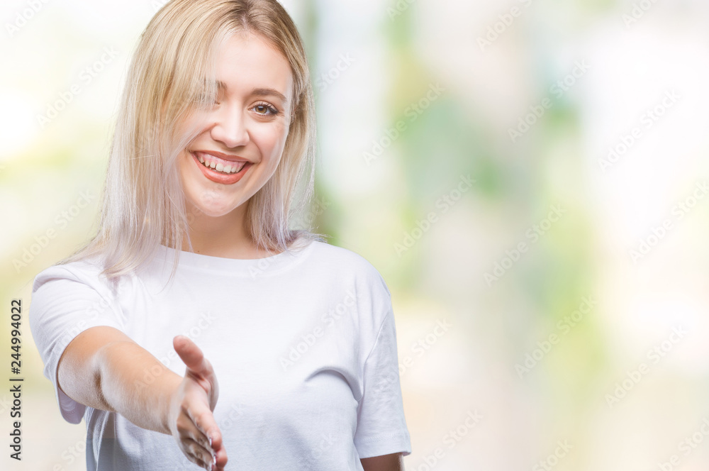 Young blonde woman over isolated background smiling friendly offering handshake as greeting and welcoming. Successful business.