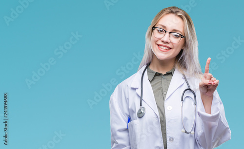 Young blonde doctor woman over isolated background showing and pointing up with finger number one while smiling confident and happy.