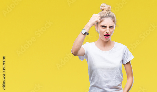 Young beautiful blonde woman wearing white t-shirt over isolated background angry and mad raising fist frustrated and furious while shouting with anger. Rage and aggressive concept. © Krakenimages.com