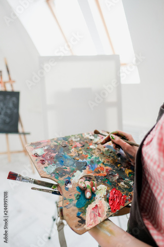 Young beautiful girl painter in a white studio draws on an easel on canvas.