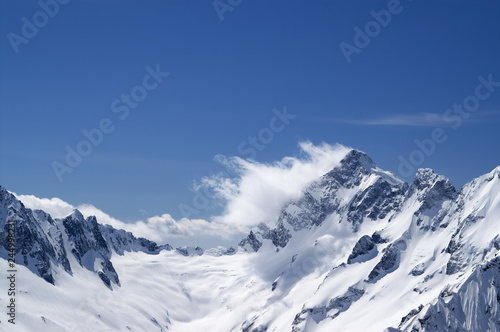 Winter snowy mountains in clouds and beautiful blue sky
