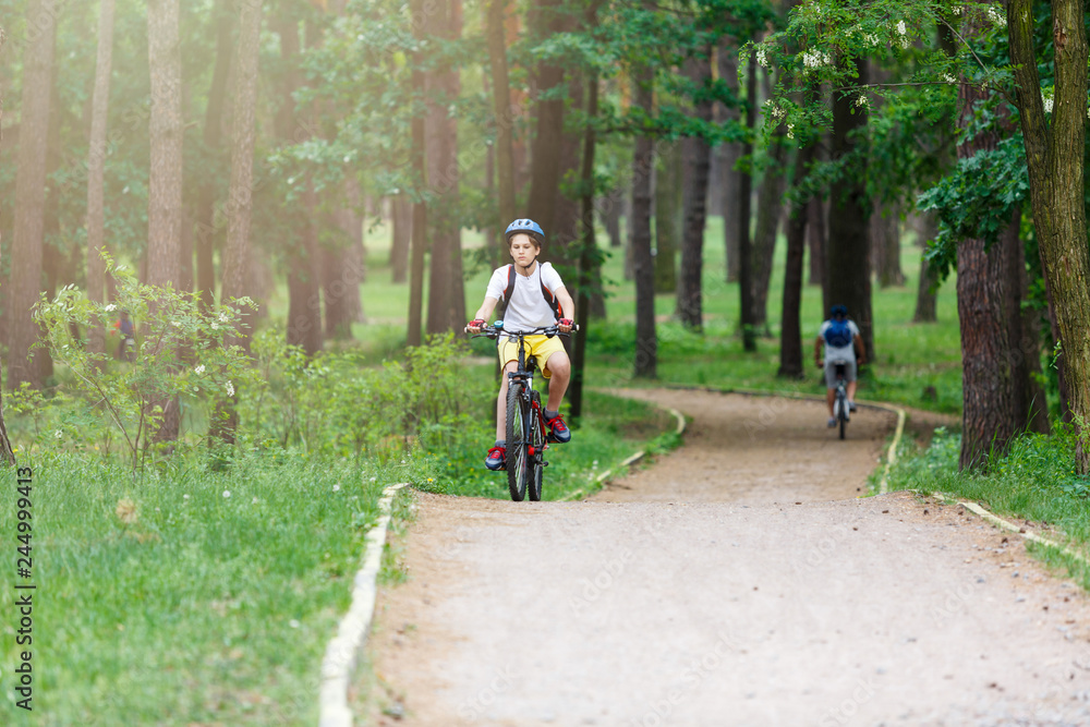 Obraz premium Child teenager in white t shirt and yellow shorts on bicycle ride in forest at spring or summer. Happy smiling Boy cycling outdoors. Active lifestyle, hobby
