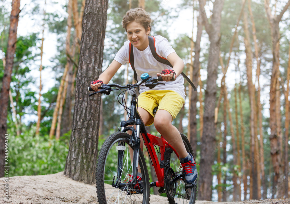 Obraz premium Child teenager in white t shirt and yellow shorts on bicycle ride in forest at spring or summer. Happy smiling Boy cycling outdoors Active lifestyle, hobby