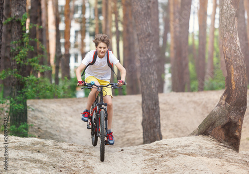 Child teenager in white t shirt and yellow shorts on  bicycle ride in  forest at spring or summer. Happy smiling Boy cycling outdoors Active lifestyle, hobby © Natali