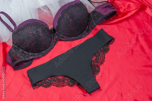 Women's sexy lingerie black and purple underwear: bra and panties on a red silk background. Valentine's day marriage proposal. The concept of the present and love