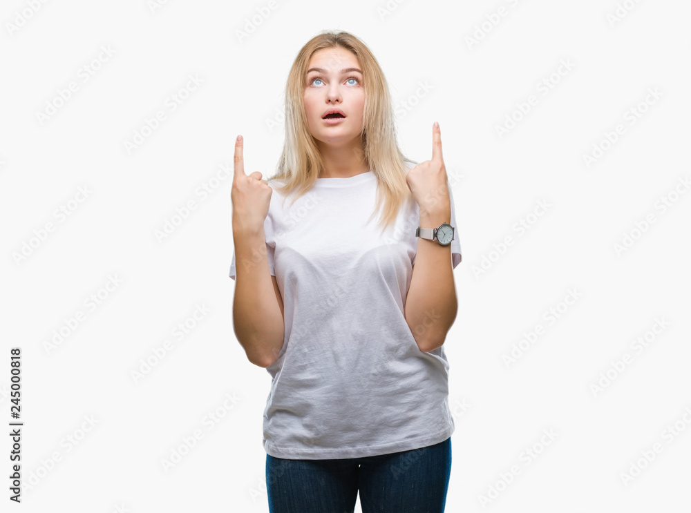 Young caucasian woman over isolated background amazed and surprised looking up and pointing with fingers and raised arms. Young caucasian woman over isolated background amazed and surprised looking up and pointing with fingers and raised arms.