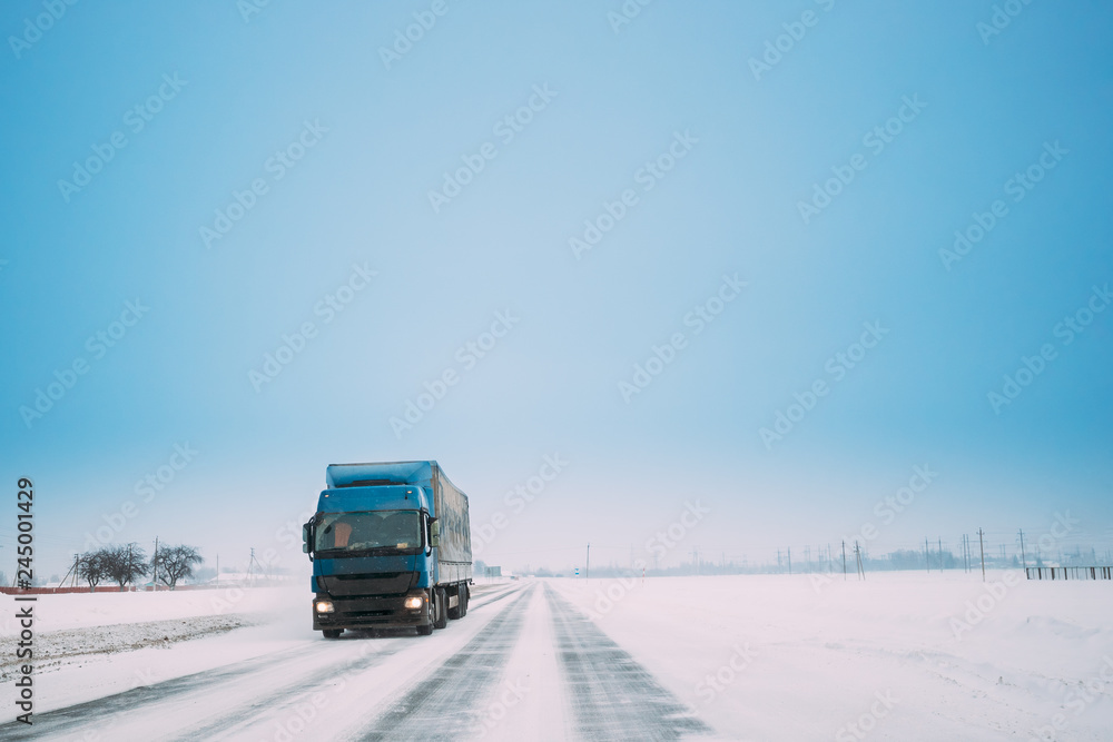 Blue Truck Or Tractor Unit, Prime Mover, Traction Unit In Motion On Winter Snowy Road, Freeway. Asphalt Motorway Highway During Snowfall. Business Transportation And Trucking Industry