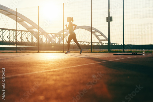Silhouette of sportive woman running on the court early in the morning at summertime.