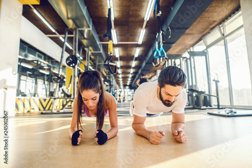 Dedicated sporty couple doing planks. Gym interior.