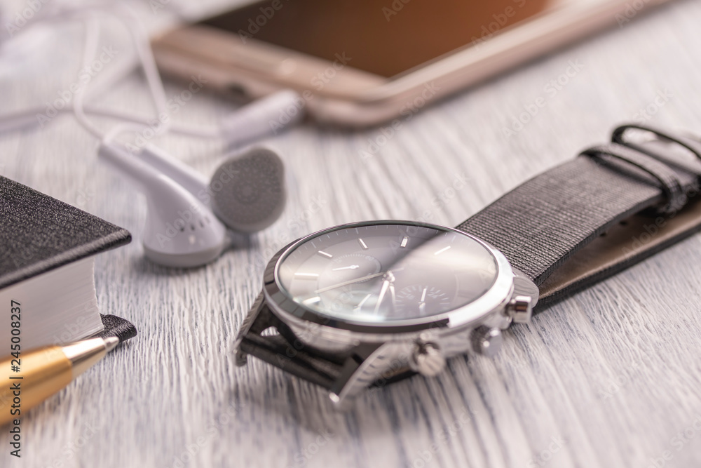 Wrist watch, mobile phone with headphones and a notebook with a pen on an old white office desktop and cafe Wrist watch, mobile phone with headphones and a notebook with a pen on an old white office desktop and cafe
