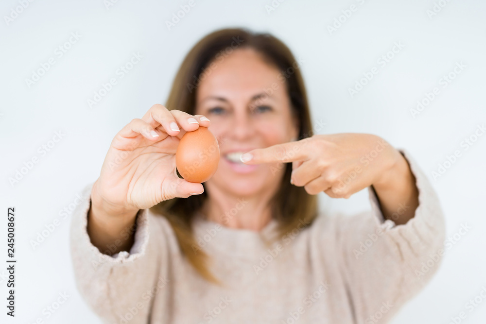 Middle age woman holding fresh egg over isolated background very happy pointing with hand and finger Middle age woman holding fresh egg over isolated background very happy pointing with hand and finger