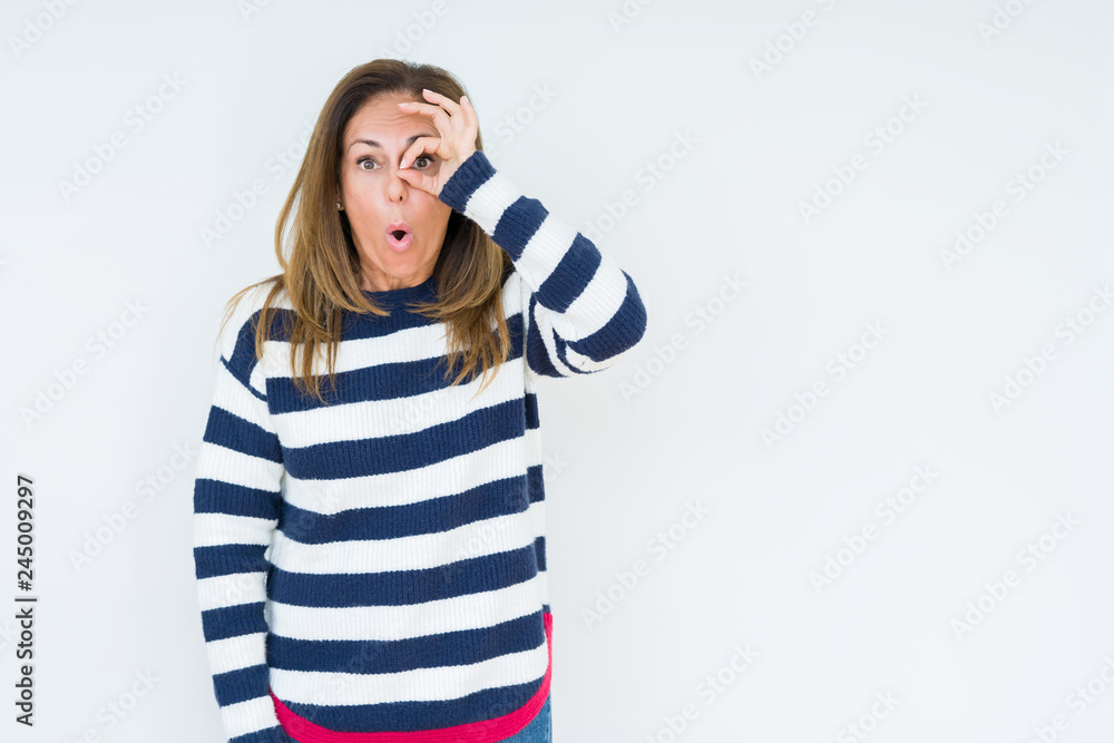 Beautiful middle age woman wearing navy sweater over isolated background doing ok gesture shocked with surprised face, eye looking through fingers. Unbelieving expression. Beautiful middle age woman wearing navy sweater over isolated background doing ok gesture shocked with surprised face, eye looking through fingers. Unbelieving expression.