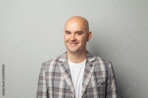 Cute bald man in a jacket and t-shirt shows against a gray wall