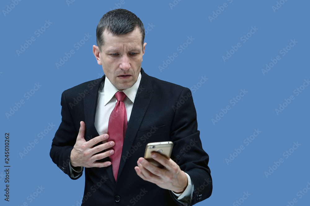 businessman looking at the phone and holding his hand in surprise at the heart. blue background. businessman looking at the phone and holding his hand in surprise at the heart. blue background.
