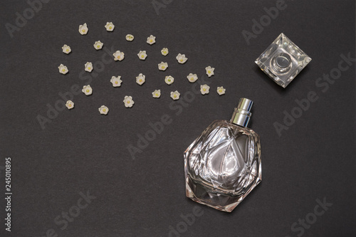 Bottle of perfume and lily of the valley flower buds on black background. Perfumery, fragrance, cosmetic concept. Spring or summer composition. Flat lay, top view, copy space